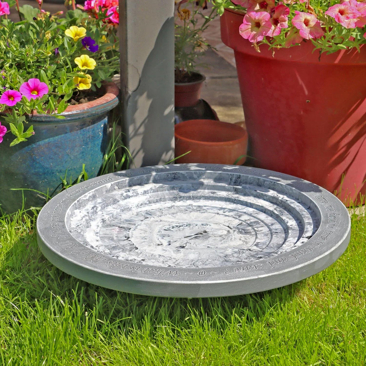 Shenstone Theatre Bird Bath and Drinker. Decorative stone bird bath in a garden setting with potted flowers.