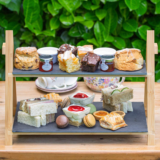 Barnsdale Afternoon Tea from The Helenium Tea Room at Barnsdale Gardens. Two-tiered serving tray with assorted finger foods on a wooden table outdoors.